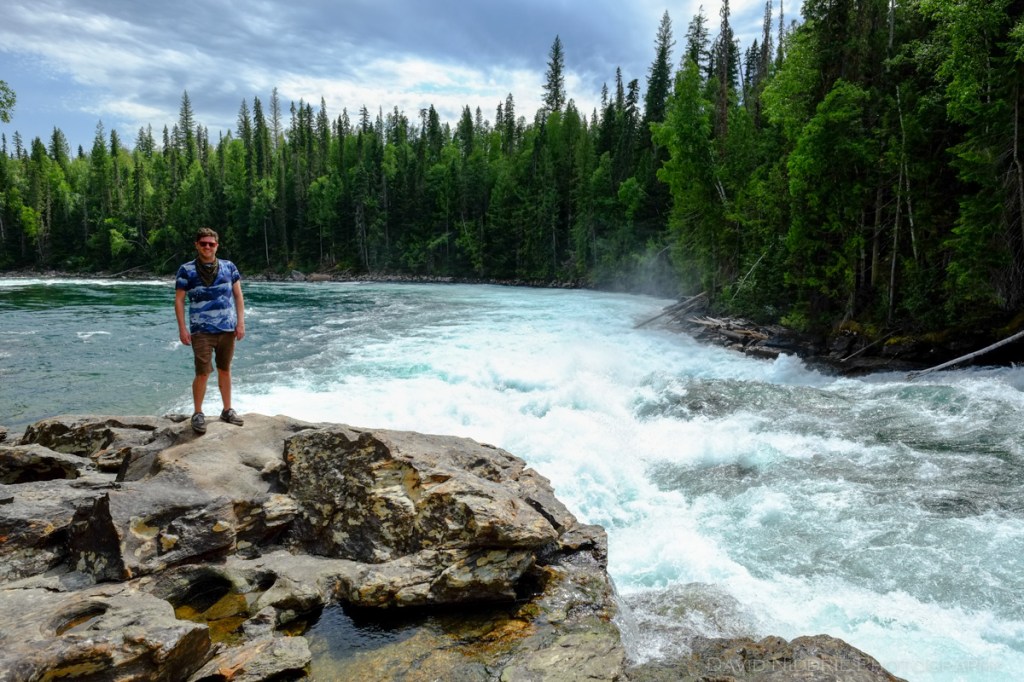 A man poses next to the whitewater of a rushing river.