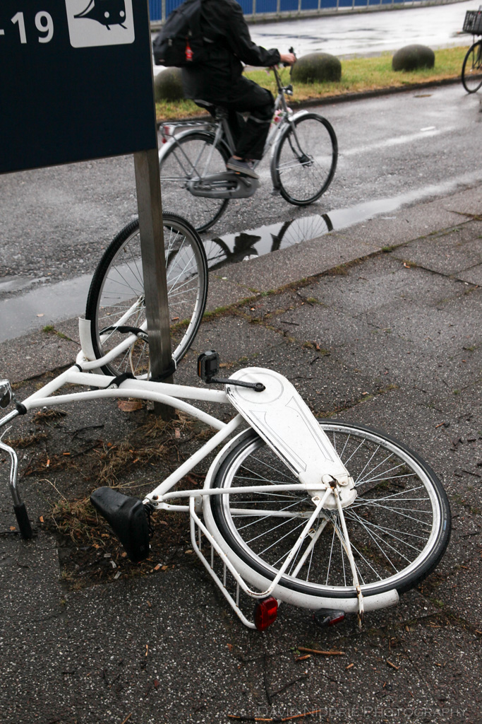 A white bike has fallen over while parked on the street in Amsterdam.
