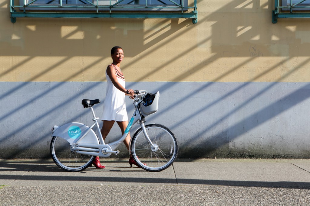 A woman walks through Gastown, Vancouver with a Mobi bike share bicycle