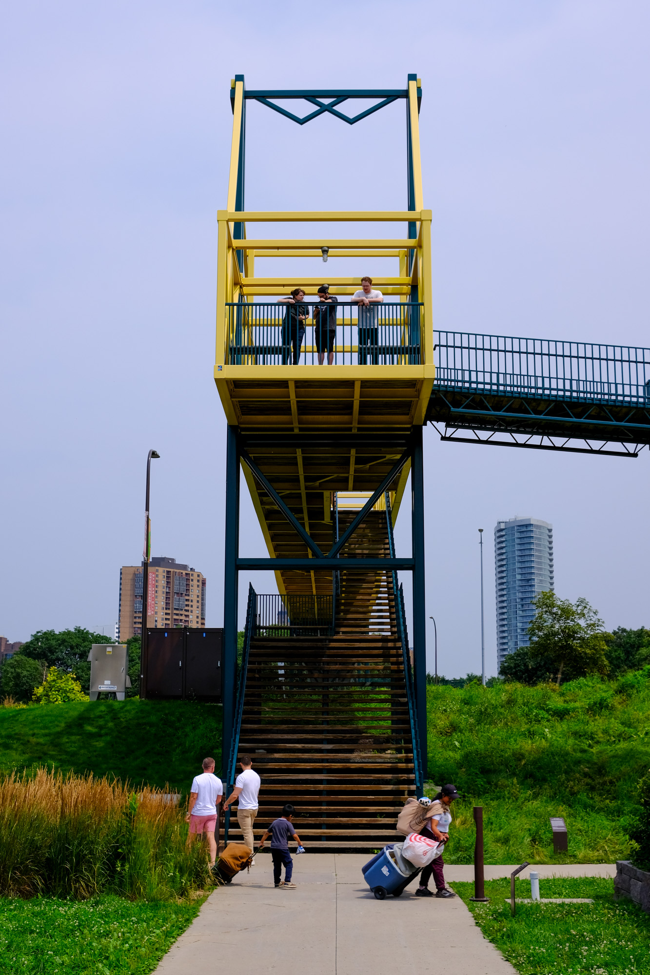 Three people look out from a bridge deck to some other people people