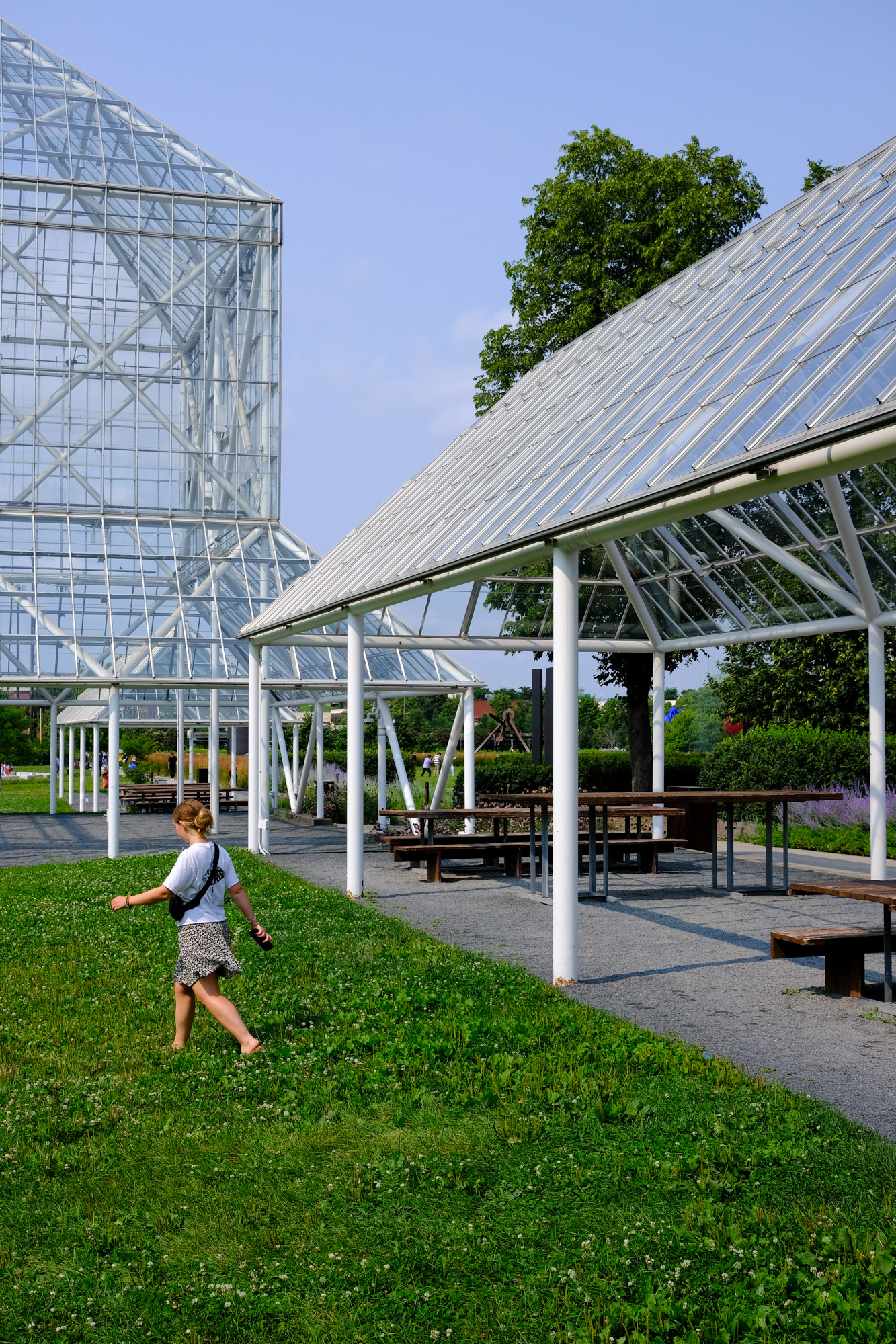 A glass and steel structure and pavilion towers overhead as a young woman walks past.