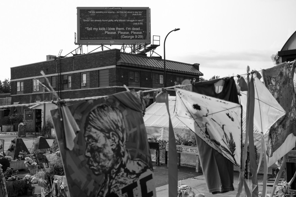 A rooftop sign above a city intersection reads "tell my kids I love them, I'm dead, please please please" - a quote from George Floyd who was killed by police on this spot in 2020.
