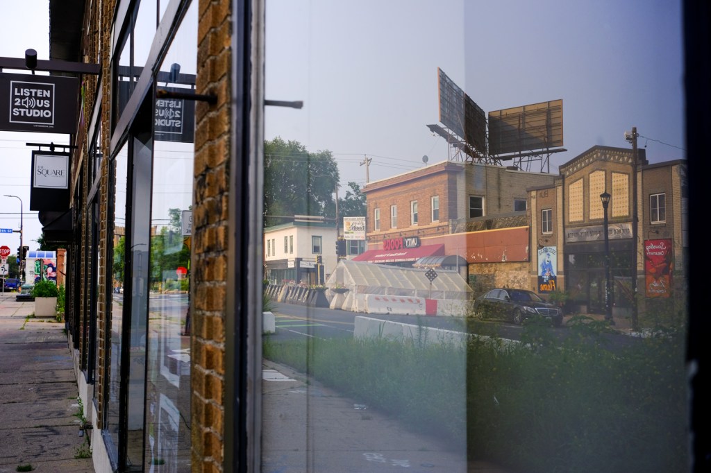 George Floyd Square is shown in a window reflection from a storefront across the street. 
